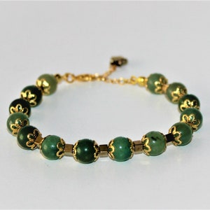May include: A green gemstone bracelet with gold accents. The bracelet is made of round beads with a floral design.