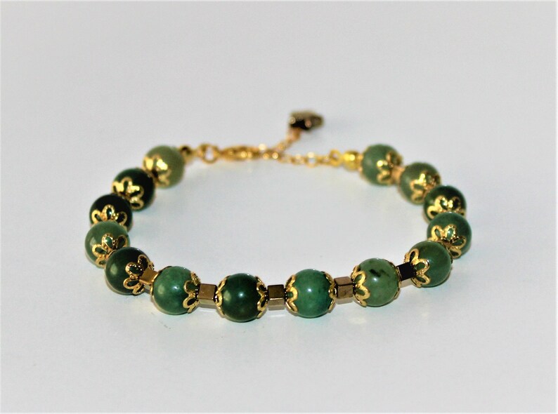 May include: A green gemstone bracelet with gold accents. The bracelet is made of round beads with a floral design.