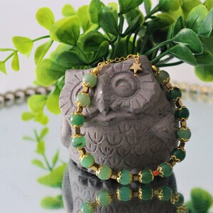 May include: A green gemstone bracelet with gold accents and a small gold star charm. The bracelet is wrapped around a gray owl figurine.