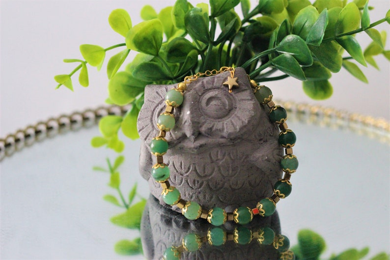 May include: A green gemstone bracelet with gold accents and a small gold star charm. The bracelet is wrapped around a gray owl figurine.