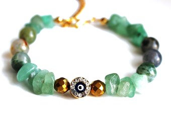 May include: A green stone bracelet with a gold evil eye charm. The evil eye charm is surrounded by clear rhinestones.