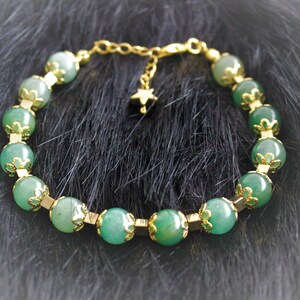 May include: A green gemstone bracelet with gold accents and a star charm. The bracelet is made of round beads with a delicate floral design.