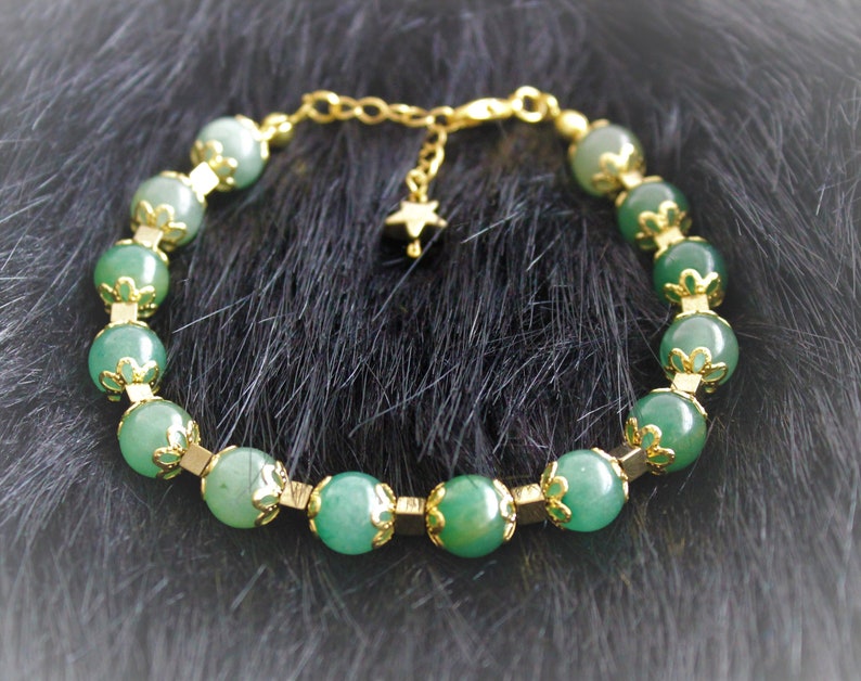 May include: A green gemstone bracelet with gold accents and a star charm. The bracelet is made of round beads with a delicate floral design.