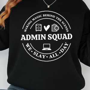 Puede incluir: Sudadera negra con un gráfico circular blanco que dice "MAKING MAGIC BEHIND THE SCENES ADMIN SQUAD WE SLAY ALL DAY". El gráfico incluye iconos de un archivador, un corazón, un reloj y un portátil. La sudadera tiene mangas largas.