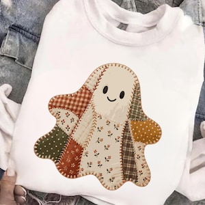 Può includere: Una felpa bianca a maniche lunghe con una grafica centrale raffigurante un fantasma realizzato con vari motivi di tessuto patchwork. Il design del fantasma include colori beige, arancione, verde e marrone con stampe floreali, a quadri e a pois.