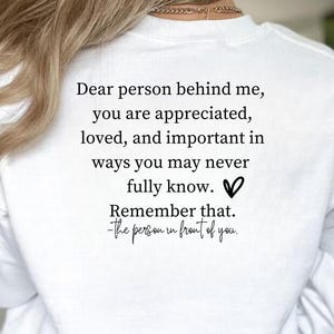 May include: White sweatshirt with black text that reads: "Dear person behind me, you are appreciated, loved, and important in ways you may never fully know. Remember that. -The person in front of you."