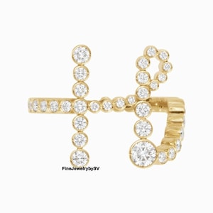 May include: A gold ring shaped like the letter "H", set with multiple clear, round gemstones. The ring's band is also decorated with smaller gemstones. The text "FineJewelrybySV" is visible.