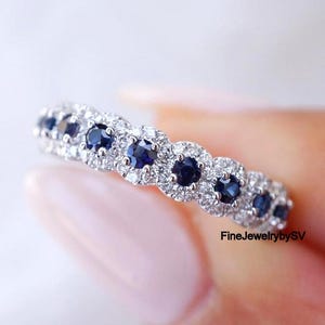 Può includere: Un anello d'argento con una serie di pietre preziose blu scuro, ciascuna circondata da pietre chiare più piccole. L'anello è presentato su uno sfondo morbido e chiaro. Il testo "FineJewelrybySV" è visibile.
