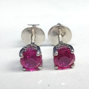 May include: A pair of stud earrings featuring round, faceted, vibrant pink stones set in silver-toned metal prongs with flat circular backings. The text FineJewelrybySV is visible above the left earring. These earrings have a classic design.