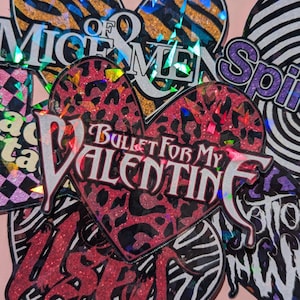 Op de afbeelding: Een verzameling holografische stickers in de vorm van een hart met verschillende bandnamen, waaronder "Of Mice & Men", "Bullet For My Valentine", "Spiritbox" en "The Stone Roses".