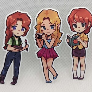 May include: Three cartoon character stickers with different hairstyles and outfits. The first character is wearing a green shirt, blue jeans, and holding a paintbrush and a palette. The second character is wearing a blue shirt, a pink skirt, and holding a camera. The third character is wearing a yellow shirt, a black skirt, and holding a book with an apple on the cover.