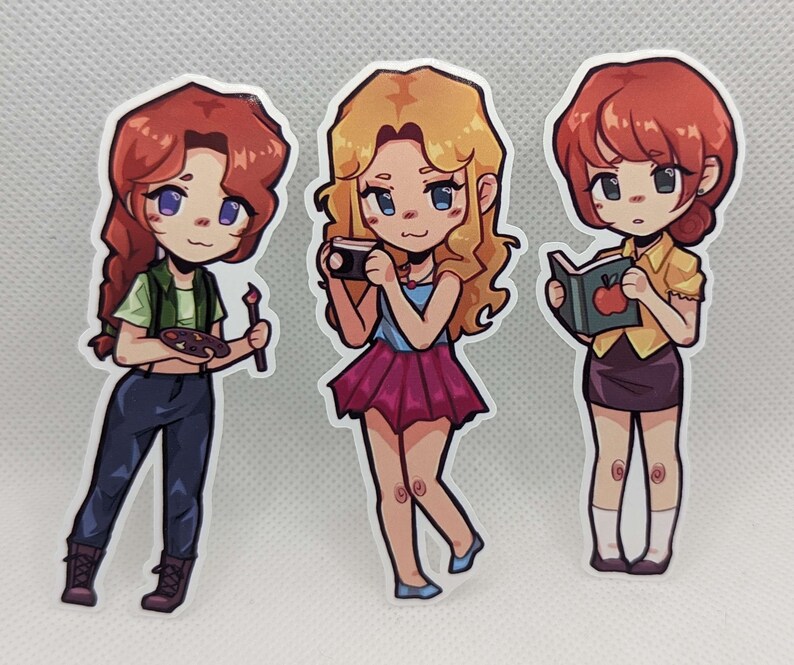 May include: Three cartoon character stickers with different hairstyles and outfits. The first character is wearing a green shirt, blue jeans, and holding a paintbrush and a palette. The second character is wearing a blue shirt, a pink skirt, and holding a camera. The third character is wearing a yellow shirt, a black skirt, and holding a book with an apple on the cover.