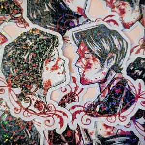 Op de afbeelding: Holografische stickers met twee figuren in profiel, hun gezichten gemarkeerd met rode accenten. De figuren staan dicht bij elkaar, met decoratieve rode krullen eromheen. De stickers hebben een glinsterende, iriserende afwerking.