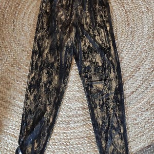 Könnte beinhalten: Schwarze Leggings mit goldenem Metallic-Muster. Die Leggings haben eine hohe Taille und eine schmale Passform. Der Stoff hat ein strukturiertes Aussehen mit goldenen Akzenten auf der schwarzen Basis. Die Leggings liegen flach auf einer gewebten Oberfläche.