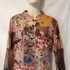 Könnte beinhalten: Eine mehrfarbige Patchwork-Bluse mit langen Ärmeln und einem Mandarinkragen. Die Bluse ist mit Pailletten verziert und hat einen Knopfverschluss am Hals.
