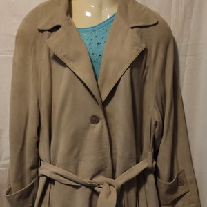 Könnte beinhalten: Eine beige Wildlederjacke mit Gürtel und einem einzigen Knopfverschluss. Die Jacke hat lange Ärmel und einen Kragen.