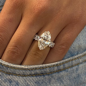 May include: A pear-shaped diamond engagement ring with a pave setting on a silver band. The ring is on a person's finger.