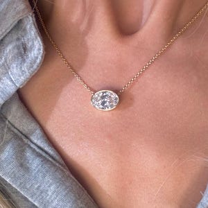 May include: A gold chain necklace with a small oval pendant featuring a cluster of clear stones.