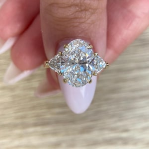 May include: A gold engagement ring with a large oval-shaped diamond center stone and two smaller triangular diamonds on either side.