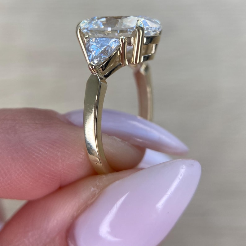 May include: A gold engagement ring with a large oval-shaped diamond and two smaller triangular diamonds on either side.
