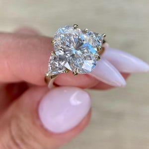 May include: A gold engagement ring with a large oval-shaped diamond and two smaller triangular diamonds on either side.