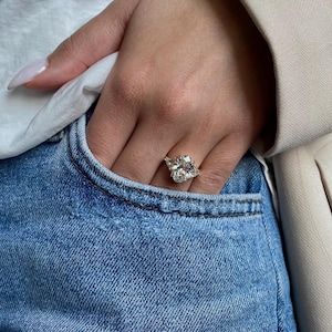 May include: A large, oval-shaped diamond engagement ring with a gold band. The ring is set with smaller diamonds on either side of the center stone.