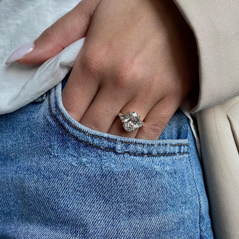 May include: A large, oval-shaped diamond engagement ring with a gold band. The ring is set with smaller diamonds on either side of the center stone.
