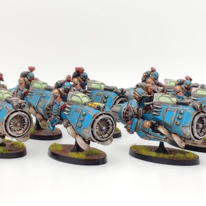 Pode incluir: Um grupo de seis naves espaciais em miniatura azuis e verdes com cavaleiros em armadura marrom e vermelha. As naves espaciais têm um design futurista com um grande motor na parte traseira.