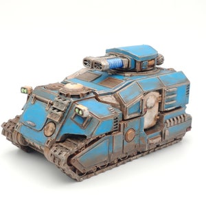 May include: A blue and brown miniature tank with a large gun turret and tracks. The tank has a weathered, battle-worn appearance.