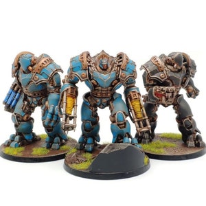 May include: Three miniature robot figures. The robots are painted in shades of blue, bronze, and black, with intricate mechanical details. They stand on circular bases with patches of green grass. The robots are posed as if ready for battle.