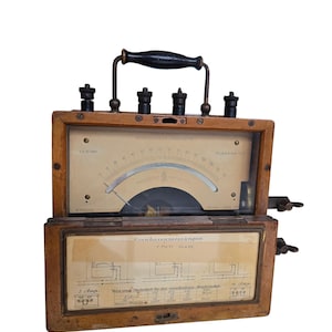 Può includere: Strumento di misurazione elettrica vintage in legno con manico nero e quadranti multipli. Il dispositivo, probabilmente un wattmetro, ha un frontale in vetro e una scala curva. Il testo "PHASENCONE WATTMEER" è visibile.