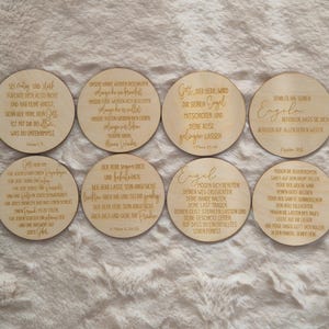 Puede incluir: Ocho posavasos redondos de madera con citas inspiradoras grabadas en alem&aacute;n. Los posavasos son de color marr&oacute;n claro y est&aacute;n dispuestos sobre una superficie suave y clara. Cada posavasos presenta una cita diferente en una fuente estilizada.