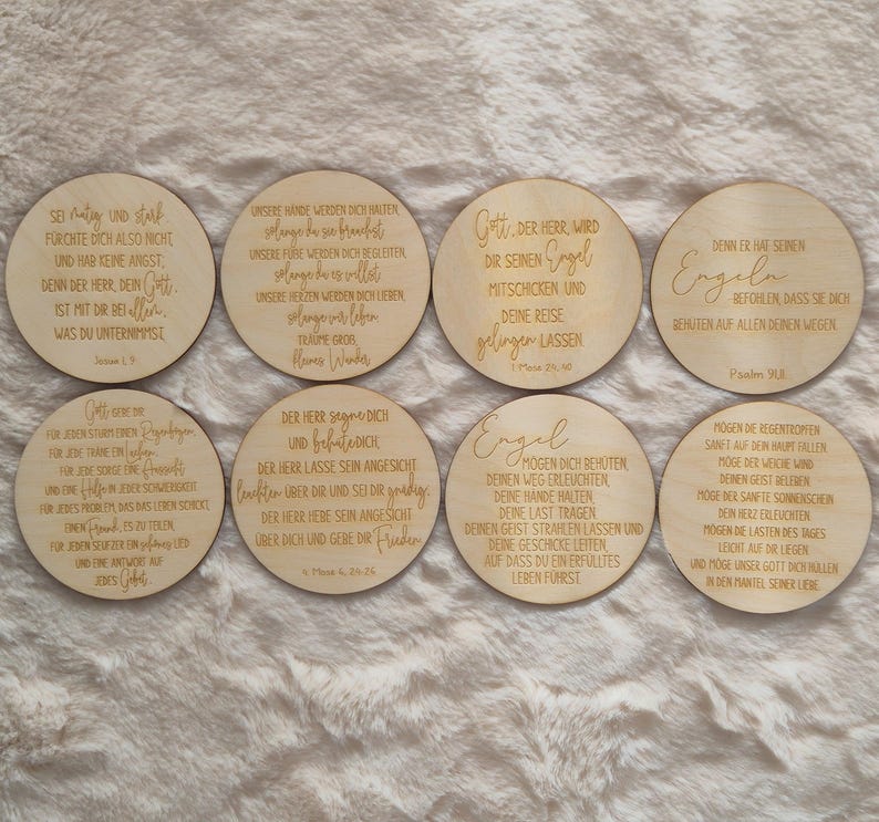 Puede incluir: Ocho posavasos redondos de madera con citas inspiradoras grabadas en alem&aacute;n. Los posavasos son de color marr&oacute;n claro y est&aacute;n dispuestos sobre una superficie suave y clara. Cada posavasos presenta una cita diferente en una fuente estilizada.