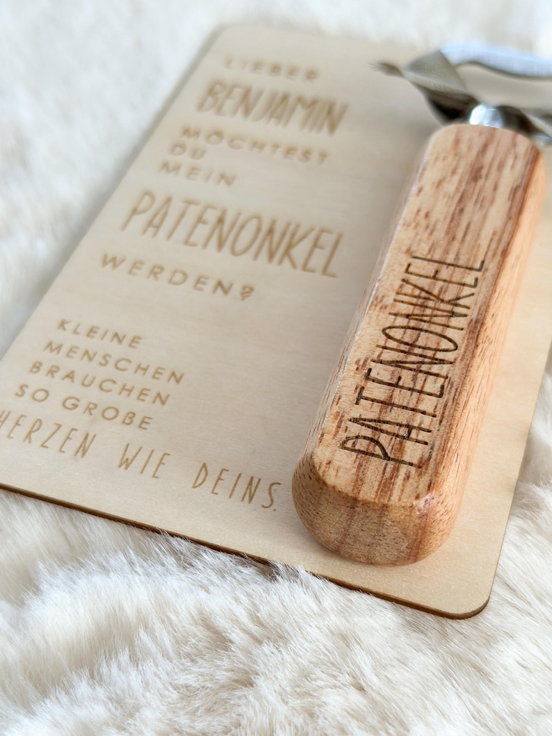 Może przedstawiać: Zestaw drewnianej tabliczki i otwieracza do butelek. Tabliczka ma wygrawerowany niemiecki tekst, w tym słowo "PATENONKEL". Otwieracz do butelek ma drewniany uchwyt z wygrawerowanym słowem "PATENONKEL".