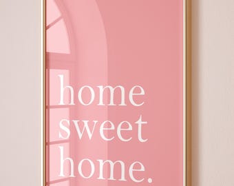 Puede incluir: Una impresión artística rosa enmarcada con las palabras "home sweet home" en blanco. La impresión está en un marco dorado y se muestra en una pared rosa claro. La imagen tiene una estética limpia y moderna.