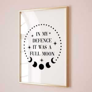 May include: A framed print with a white background and black text that reads "In my defence it was a full moon" surrounded by a circle of dots and a crescent moon design.