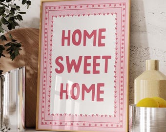 Puede incluir: Una impresión enmarcada en rosa con fondo blanco y el texto "HOME SWEET HOME" en letras rosas. El marco tiene un borde rosa y blanco con un patrón repetitivo de corazones y estrellas.