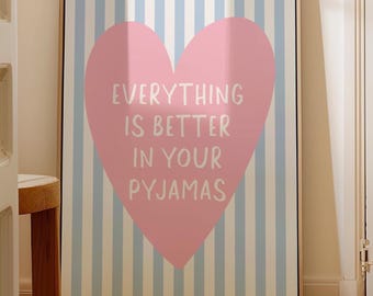 Peut inclure: Une affiche encadrée avec un cœur rose et le texte "EVERYTHING IS BETTER IN YOUR PYJAMAS". Le fond présente des rayures verticales bleues claires et blanches. Le cadre est de couleur marron clair.