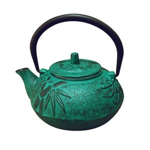 May include: A teal green cast iron teapot with a black handle and a lid with a raised design. The teapot has a bamboo design on the side.