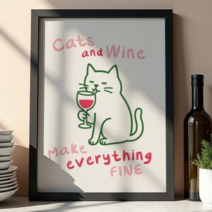 May include: A framed art print featuring a cartoon cat holding a glass of red wine. The text "Cats and Wine Make Everything Fine" is written in pink and green. The print is in a black frame and is displayed on a shelf.