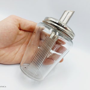 Könnte beinhalten: Ein durchsichtiger Zuckerstreuer aus Glas mit silbernem Deckel und silbernem Ausgießer. Der Streuer hat ein geripptes Design.