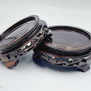 Puede incluir: Dos soportes de exhibición de madera marrón oscuro con detalles tallados de flores y volutas. Los soportes tienen una parte superior redonda y una base con tres patas. Los soportes están hechos de madera oscura y pulida.