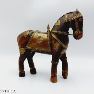 Op de afbeelding: Houten paardenbeeldje met ingewikkelde messing accenten. Het donkerbruine paard heeft een zadel en hoofdstel met goudkleurige metalen accenten. Het decoratieve stuk heeft een klassieke, vintage uitstraling.