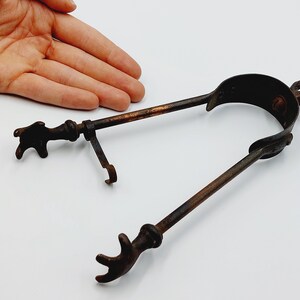 Peut inclure: Un outil de cheminée antique en métal avec une longue poignée et deux extrémités en forme de griffes. L'outil est conçu pour soulever et déplacer les bûches dans un foyer.