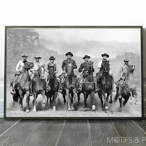 以下が含まれることがあります： 砂ぼこりが舞う平原を、帽子をかぶった7人のカウボーイが馬に乗って駆け抜ける白黒写真。カウボーイたちは皆前を見つめ、馬は勢いよく駆けている。