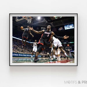 May include: A basketball player wearing a black and red jersey with the number 3 and the word "HEAT" on it jumps to dunk the ball. The player is wearing black shorts and black sneakers. The player is in mid-air and has his arms extended above his head. The player is surrounded by other players and fans.