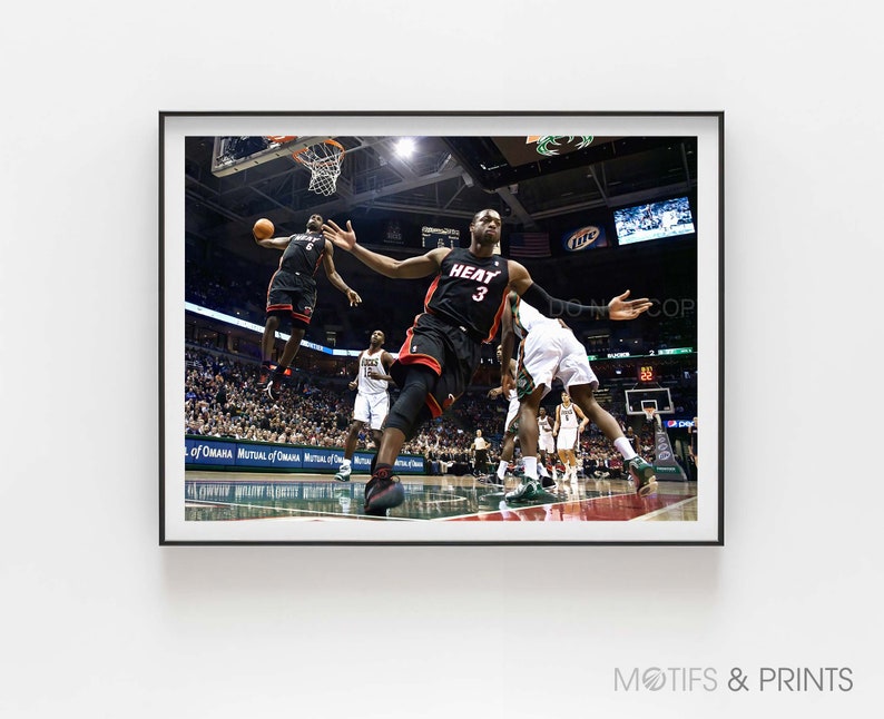 May include: A basketball player wearing a black and red jersey with the number 3 and the word "HEAT" on it jumps to dunk the ball. The player is wearing black shorts and black sneakers. The player is in mid-air and has his arms extended above his head. The player is surrounded by other players and fans.