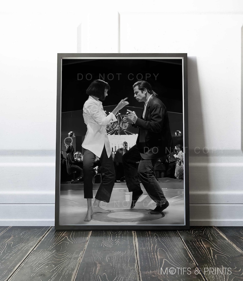 May include: Black and white photograph of a man and woman dancing in a nightclub. The man is wearing a suit and the woman is wearing a white shirt and black trousers. The couple are dancing in the centre of the dance floor, with other people in the background.
