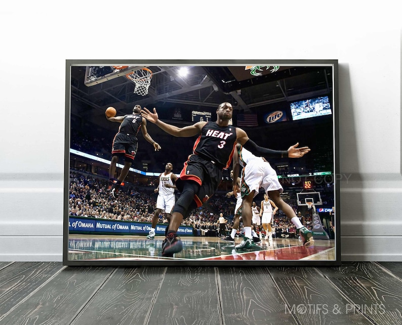 May include: A basketball player in a red and black jersey with the number 3 and the word "HEAT" on the front jumps to dunk the ball. The player is wearing black shorts and black knee pads. The player is in mid-air with his arms extended and the ball in his right hand. The player is surrounded by other players and fans in the background.