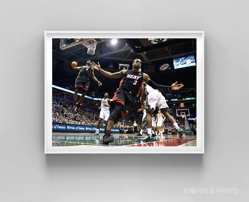 May include: A basketball player in a black and red jersey with the number 3 and the word "HEAT" on the front jumps to dunk the ball. The player is wearing black shorts and black sneakers. The player is in mid-air with his arms outstretched. The background is a basketball court with a crowd of people in the stands.